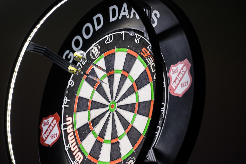 Zwei Pfeile stecken in einem Dartboard, umringt von einem beleuchteten Rahmen mit der Aufschrift „GOOD DARTS“.