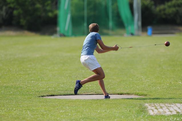 Athlet wirft mit einer Wurfmaschine eine Kugel auf einer Sportanlage mit grünem Rasen.
