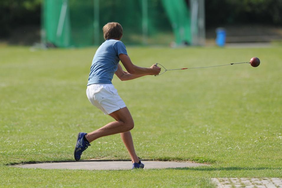 Athlet wirft mit einer Wurfmaschine eine Kugel auf einer Sportanlage mit grünem Rasen.
